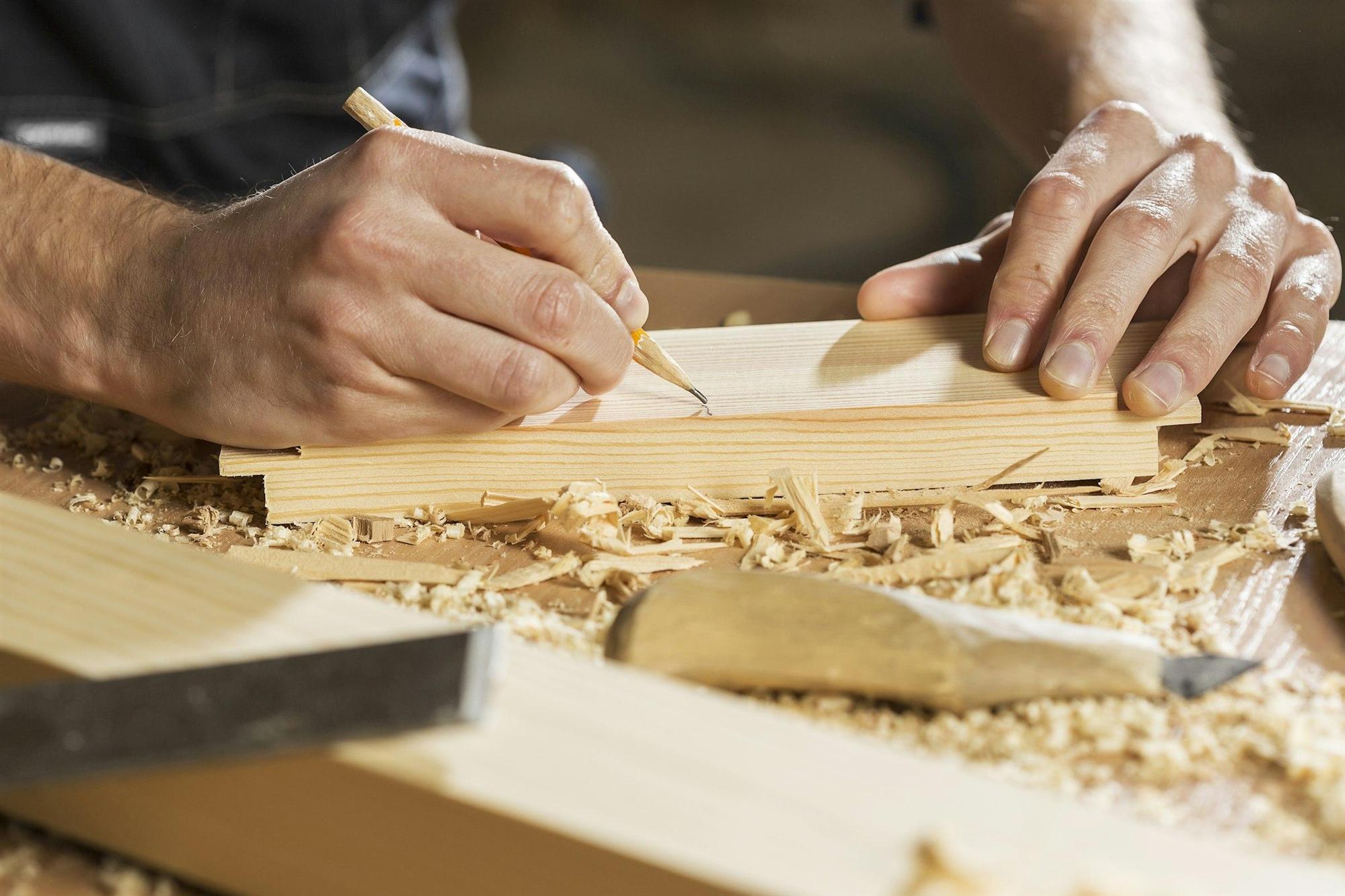 A carpenter marks a cut line on a board with a pencil